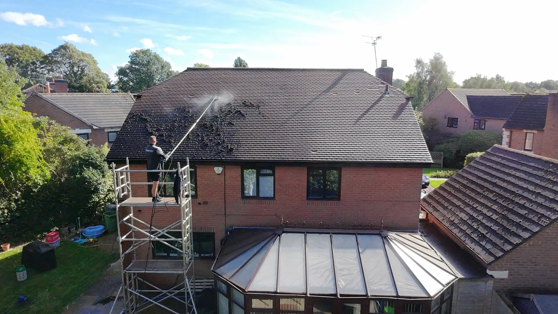 Cleanest Exteriors technician on an access tower lifting moss off a tiled roof with a low-pressure telescopic lance