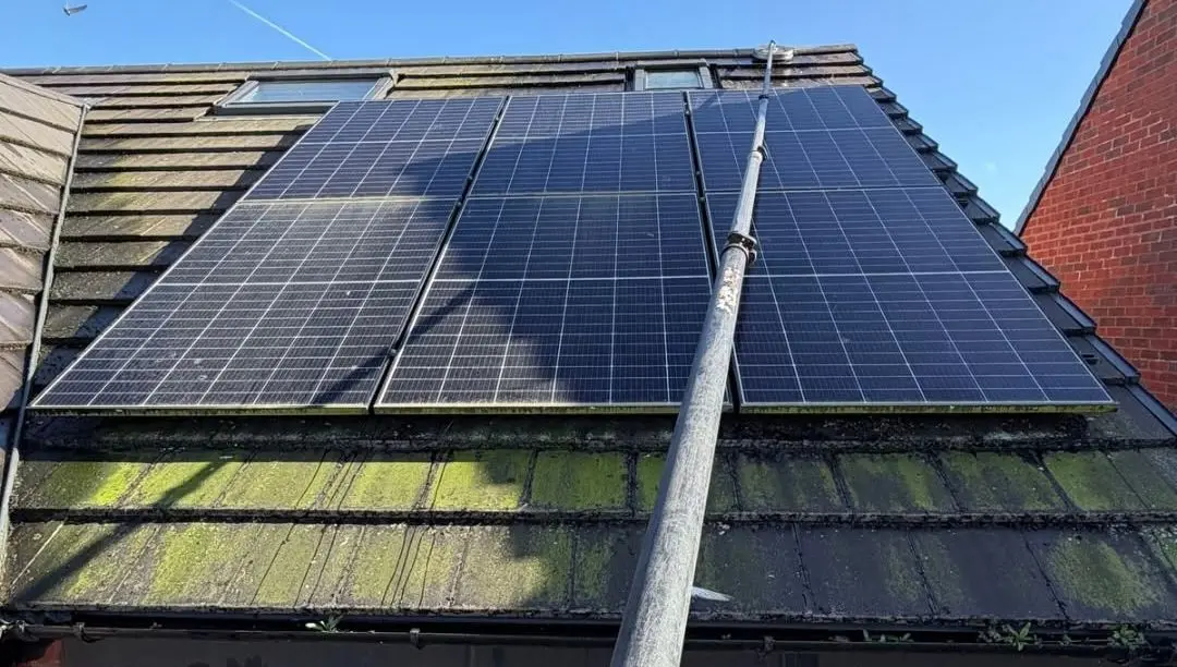 Tiled roof around solar panels before cleaning, thick green moss on the lower courses
