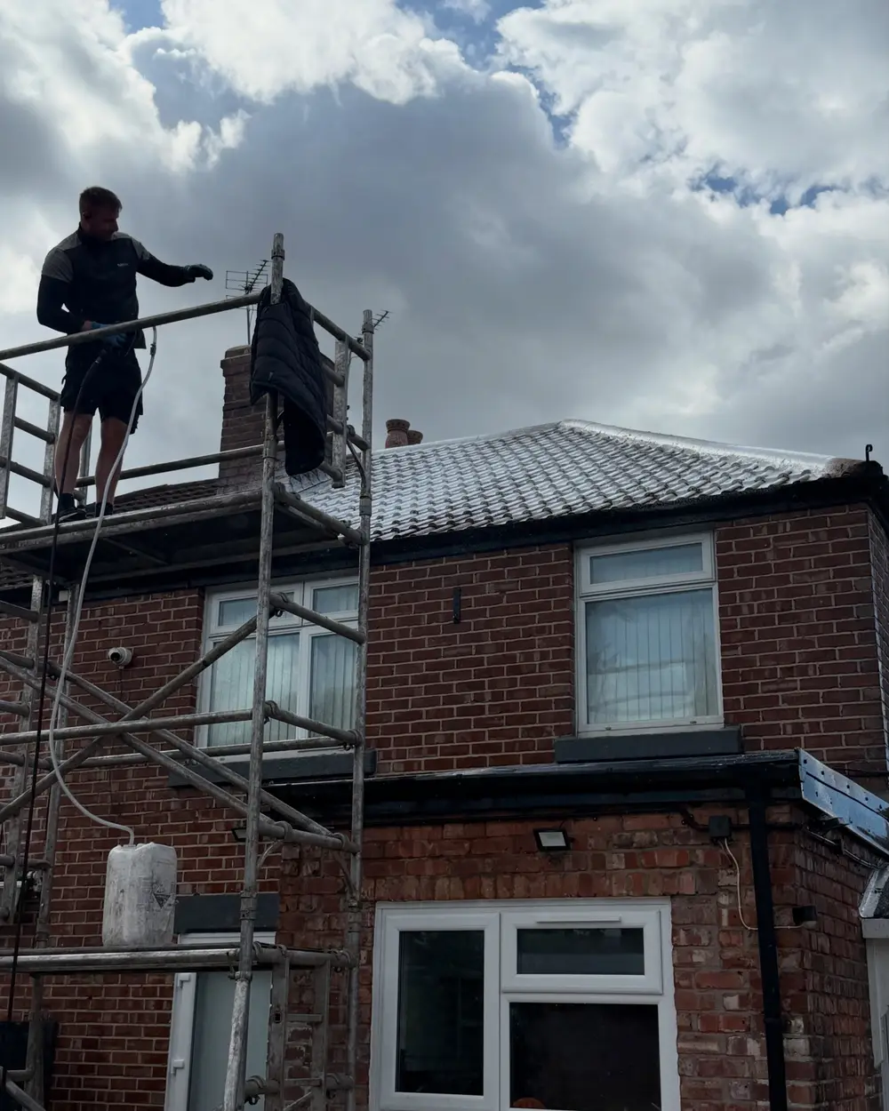 Technician working from a scaffold tower to clean the roof of a red brick house